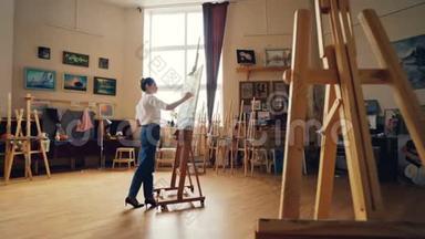 严肃的年轻女画家在艺术学校的教室里用丙烯酸<strong>颜料画</strong>画画画，画架和